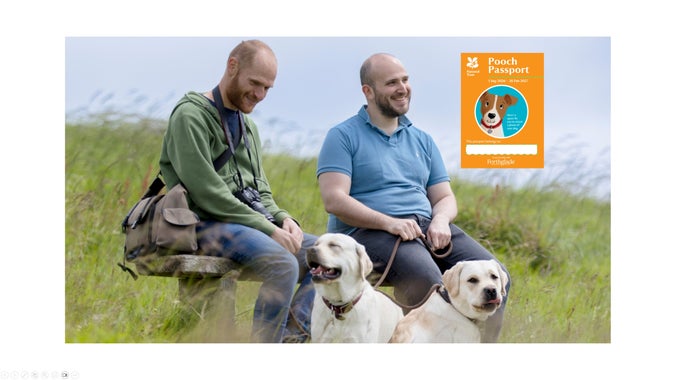 Two men resting on a bench with their dogs at their feet in long grass with an orange Pooch Passport icon